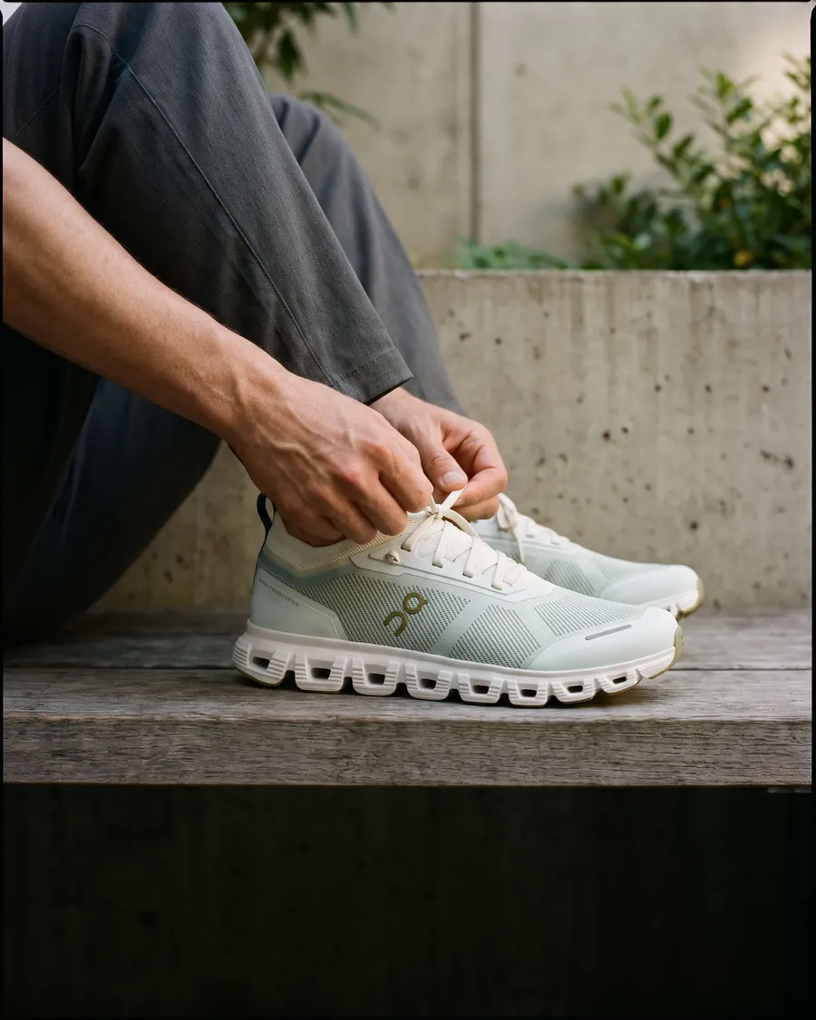 Hands tying pale mint Cloud 6 Versa trainers beside a city bench